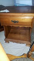 Front view of a wooden nightstand showing top surface, single drawer with metal handle, and lower open shelf.