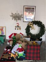 Overview photo showing various holiday decorations including Christmas wreath, plush toys, rug, framed art, and other items.