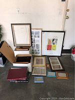 Various assorted picture frames and photo albums arranged together on floor and against wall, showcasing different sizes and styles.
