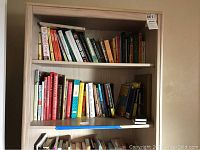 Books arranged on two shelves of a wood bookcase, showing a collection of various sized books in used condition.