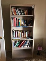 Front view of wooden bookcase filled with assorted books, showing overall condition and four shelves.