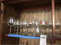 Shelved collection of 22 vineyard themed wine glasses including 21 stemmed glasses and 1 tumbler with visible labels and decals