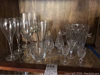 Full view of all items including wine glasses, liqueur glasses, salt and pepper shakers, tumbler, and ice bucket on wood shelf.