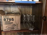 Box of Libbey flute glasses with additional etched Thornton Winery Jazz Series glasses beside it on a wooden shelf.