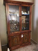 Front view of wooden China cabinet with glass upper doors showing shelves inside with glassware and lower wood doors closed.