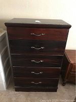 Front view of five drawer wooden dresser showing scratches and metal handles.