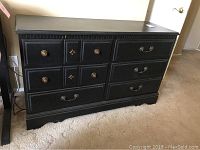 Full view of the black 6 drawer dresser sitting on carpet, showing overall condition and shape.