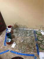 Photo of 27 assorted drinkware items arranged on floor, includes beer mugs, coffee cups, glasses, and tumblers.