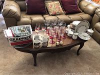 View of entire Christmas dish set and glassware on wooden coffee table including plates, bowls, coffee cups, wine glasses, salt and pepper shakers, cloth napkins, cookie cutter box.