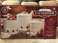 Box showing set of three ceramic canisters labeled Onions, Potatoes, and Garlic with ventilation holes, white glazed finish