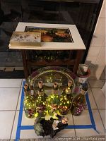 Image showing arranged lot items on tiled floor including five lighted green wine bottles in front, a platter and two framed vineyard prints on top of a wine rack, and a grape figurine on the floor