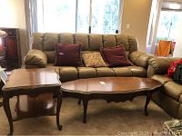 Wooden coffee table and end table set shown in living room next to sofa, tables are brown with curved legs and show some surface marks and scratches.