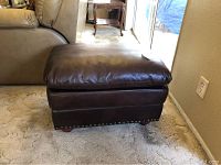 Brown leather ottoman positioned next to a beige couch on carpet.