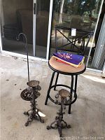 Photo showing two wrought iron candle holders, a metal bar chair with tan cushion, and two folded flags on the chair seat