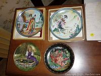Four vintage collector plates on tabletop showing detailed artwork of Asian motifs, a garden scene and a carriage scene.