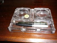 Top view of clear glass double inkwell with two vintage fountain pens resting in front.