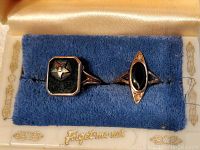 Two antique gold rings displayed side by side on a blue velvet cushion inside a vintage ring box labeled 'Forget me not'.