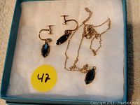 Earrings and pendant on chain shown inside blue box on white cushioned surface with yellow sticker labeled 47.