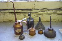 Seven assorted vintage and antique oil cans and funnels arranged on a surface with worn wooden background.