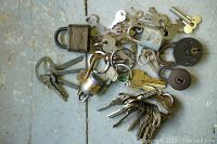 Photo showing various vintage padlocks and a large assortment of keys scattered on a wooden surface.