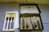 Photo of three chisels with translucent yellow and red handles lying outside the box on a surface.