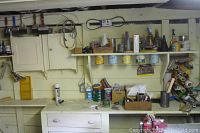 Full view of workbench and shelving with paintbrushes, paint cans on shelf, and various containers and tools on countertop.