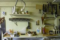 Wide shot showing pegboard with mounted hand tools including saws, wrenches, pliers, and shelves holding various items including bottles and small tools.