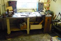 Photo of vintage hand tools spread on a wooden table and drawers underneath, showing general setup and accumulation of various tools and vintage items.