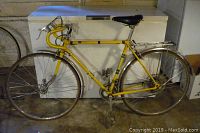 Side profile of vintage yellow BRC road bicycle showing frame, wheels, handlebars, fenders, and rear luggage rack in a garage setting.