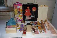 Wide shot showing assortment of vintage Barbie dolls, doll case, boxed doll and accessories on a table