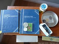 Top view of the lot including four blue coin albums labeled Canadian Small Cent Collection and Canadian Dime Collection, a green Australian coin holder, loose coins, a small white box, a small yellow and white jar, and a round metal tray.