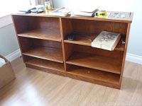 Full view of the low wooden bookshelf standing on a hardwood floor in a room with white trim walls. Various small items are on top of the bookshelf.