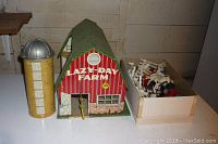Tin lithographed 'Lazy-Day Farm' barn with attached yellow silo and box of plastic accessories.