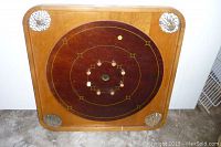 Front side of vintage crokinole board showing circular scoring surface with decorative inlaid wood and cracked corner decorations.