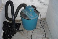 Full view of vintage Craftsman wet-dry vac with hose attached, placed on concrete floor near pegboard wall.