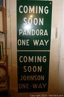 Two green plastic signs with white text, 'COMING SOON PANDORA ONE WAY' and 'COMING SOON JOHNSON ONE-WAY' displayed vertically on a wall.