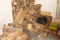 Image showing a large stack of split firewood logs stacked in the corner with some boxes and wooden planks in front.