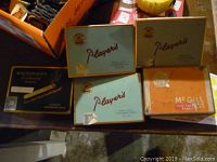 Photo showing four Player's vintage tobacco tins in light green color with brown and gold accents, stacked and positioned closely together, along with one McGill tin in orange.