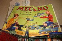 Photo of two vintage Meccano instruction booklets featuring illustrations of boys playing with Meccano models including a crane and a vehicle.