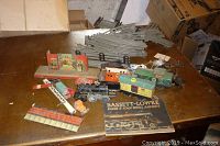 Overview of wooden table showing assortment of vintage toy trains, tracks, a signal gate and a Bassett-Lowke booklet