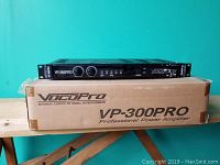 Front view of VocoPro VP-300PRO amplifier mounted above its original cardboard box with model and branding visible.