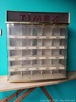 Front view of Timex showcase display case with multiple small compartments for watches and large 'TIMEX' logo on wood panel at top.