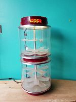 Full front view of the electric Zippo lighter display case showing all shelves inside two clear cylindrical compartments and the red top and base with Zippo branding.