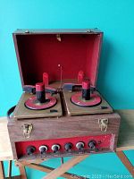 Front view of open wooden case displaying two 45 RPM turntables with red stacking spindles and built-in amplifier control panel.