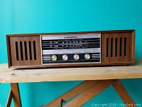 Front view of Concerto AM-FM radio showing wood casing, dual speakers, radio dial with AM and FM frequencies, and four control knobs.