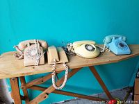Four vintage telephones on wooden bench, three rotary dial and one push-button, blue phone repainted
