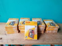 Group of 20 packs of Kodak photo paper stacked on wood surface against blue background