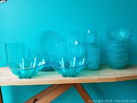 Front view of blue plastic dishware including plates, cups, bowls, decorative oyster-shaped bowls, and a pitcher with bubble texture.