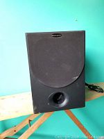 Front view of one black Dahlquist subwoofer with grille and bass port visible