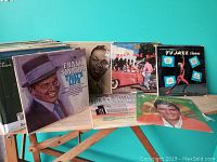 Photo showing a box of mixed vinyl records including a Frank Sinatra album, Nat King Cole album, a rock and roll compilation, and a TV Jazz Themes album.